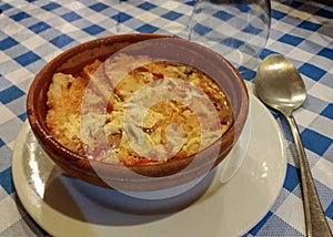 Rustic bowl of Castilian soup.  Onion soup on a table with blue checkered tablecloth.