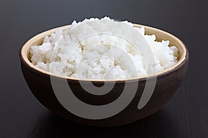 Rustic bowl of cooked white rice on dark surface photo