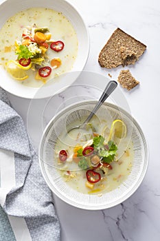 Rustic chicken soup with vegetables, noodles, lemon slice, celery leaves and fresh red chilli