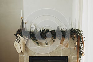 Rustic christmas fireplace with warm knitted stockings and stylish decoration on fir branches. Cozy stockings hanging on mantel in