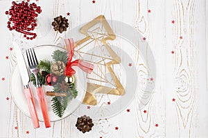 Rustic Christmas table with festive decor, cutlery on a white plate, glass, cones, fir branches on a white washed background, flat