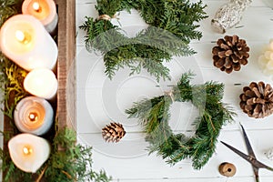 Rustic christmas wreath with candles, pine cones, scissors and ornaments on white  table, flat lay
