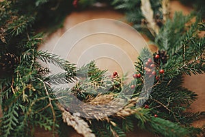 Rustic Christmas wreath detail closeup. Fir branches, pine cones, berries on wooden table. Authentic stylish still life. Making
