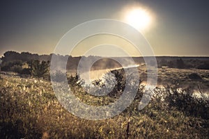 Rustic countryside scenery landscape sunrise with fog river on riverbank with sun and dramatic sky in vintage style