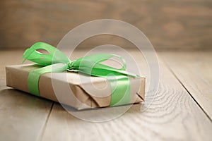Rustic craft paper gift box with green ribbon bow on wood table