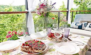 A rustic dacha-style table with a bouquet of wild flowers stands on the garden terrace, awaiting guests. Glasses on a set table