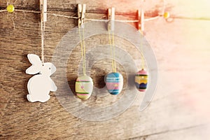 Rustic Easter background: Vintage painted eggs and white bunny hang on clothespins against old brown wooden wall. Holiday concept