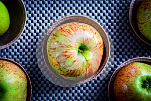 Rustic fresh apples in paper plates, on a gray tablecloth with holes, top view