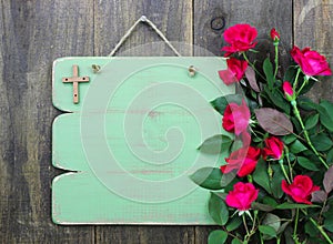 Rustic green blank sign with wooden cross and flower border of red roses hanging on wood door