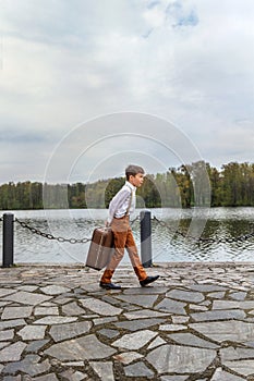 rustic guy in old-fashioned clothes paces on the pier with a huge retro old suitcase