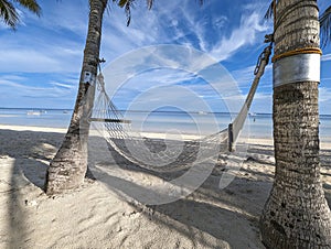 A rustic hammock tied to the two trunks of coconut palm trees. At Dumaluan Beach, Panglao Island, Bohol, Philippines