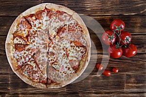 Rustic homemade pizza with salami and lots of cheese lies on a wooden table next to a bunch of red tomatoes. Autumn Farm Fair