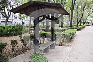 Rustic log bench with roof surrounded by bushes in park from Mexico City