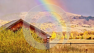 A rustic log cabin, a rainbow, and cottonwood trees with autumn foliage in a beautiful Wyoming landscape.