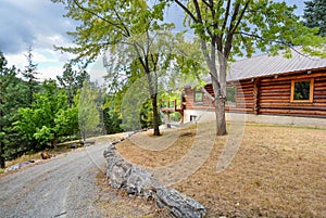 A rustic log cabin in a rural mountain setting with landscaped rocks and a hammock swing between two trees in the mountains of the