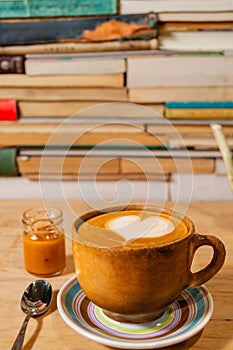 Rustic ochre cappuccino mug with caramel and Himalayan salt, shaped foam on plate, wood and book background - Taza de capuchino r photo