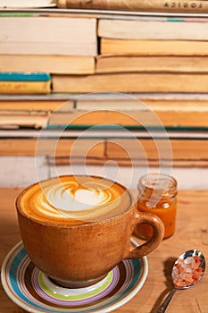 Rustic ochre cappuccino mug with caramel and Himalayan salt, shaped foam on plate, wood and book background - Taza de capuchino r photo