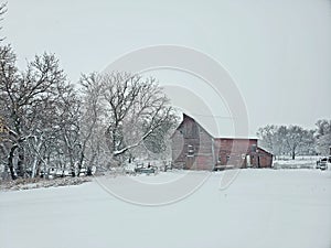 Rustic old red barn standing strong in a Nebraska winter storm with snow and ice.