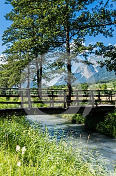 Rustic old wooden bridge over a small stream in a tree-lined alley