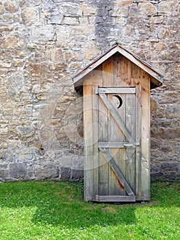 Rustic outhouse in front of vintage stone wall