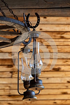 Rustic ranch chandelier made from wood wagon wheel, iron horseshoes, and lanterns, hanging from aged wood ceiling