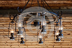 Rustic ranch chandelier made from wood wagon wheel, iron horseshoes, and lanterns, hanging from aged wood ceiling