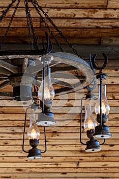 Rustic ranch chandelier made from wood wagon wheel, iron horseshoes, and lanterns, hanging from aged wood ceiling