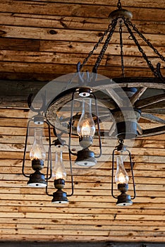 Rustic ranch chandelier made from wood wagon wheel, iron horseshoes, and lanterns, hanging from aged wood ceiling