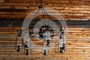 Rustic ranch chandelier made from wood wagon wheel, iron horseshoes, and lanterns, hanging from aged wood ceiling