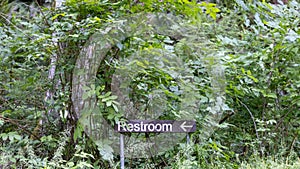 rustic restroom sign with arrow on forest path