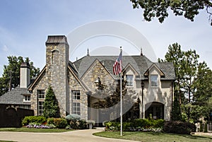 Rustic rock and brick upscale beautifully landscaped home with copper spires and chimney covers flying American flag on tall flagp