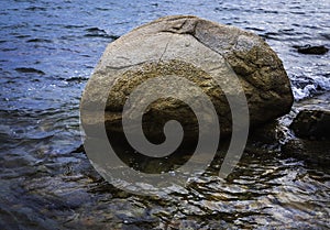 Rustic round boulder, reflections and curvy waves on the sea water