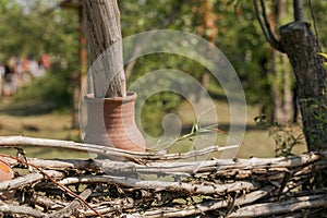 Rustic Russian traditional wicker fence with the neck of a clay pot outdoor in summer, selective focus.