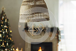 Rustic scandinavian straw decoration hanging on background of festive golden lights bokeh in modern farmhouse living room.