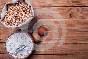 Rustic Scene with Wheat Grains, Flour in Bowl, and Eggs on Old Wooden Table. Healthy Food Concept
