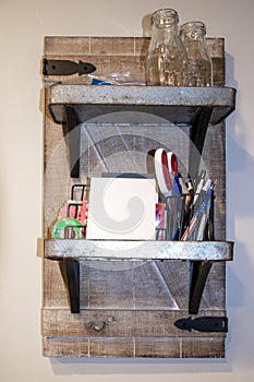 Rustic shelves with barn door backing and metal shelves hanging on wall  with tape, note pad, writing instruments and sissors