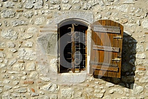 A rustic shuttered window with ornate security bars