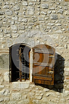 A rustic shuttered window with ornate security bars