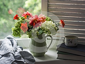 Rustic still life - autumn bouquet of hydrangeas and dahlias in a ceramic jug, books, a cup of green tea on a window with wooden