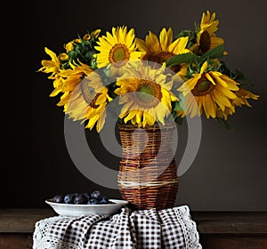 Rustic still life, sunflowers in a wicker vase and a plate with plums