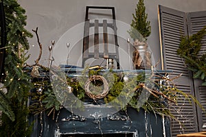 Rustic style Christmas festive decorations, fresh spruce thuja, fir branches, wreath on fireplace, sledges. Warm garland lights