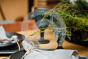 rustic style Christmas festive table, blue glasses, plates and fresh thuja branches bouquet. Eco-friendly elements