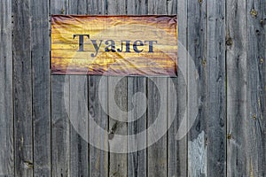 Rustic "Toilet" sign, written in Russian, on weathered wooden boards