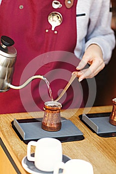 Rustic Turkish cezve, coffeepot, ibrik with boiled coffee beans, water, spices, cinnamon, salt on electric stove and wooden table.