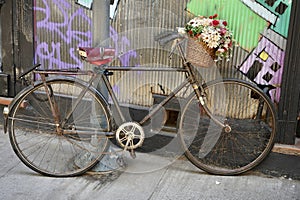 Rustic Vintage Pushbike with flowers in a basket leaning against a corrugated metal wall.
