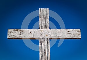 Rustic weathered wooden Memorial cross against a blue sky.
