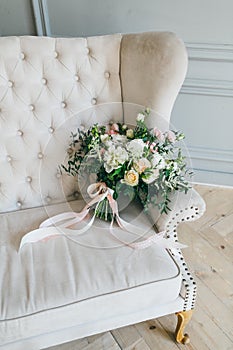 Rustic wedding bouquet with creamy roses and white carnations on a luxury cream sofa. Close-up. Side view