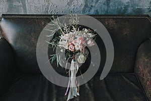 Rustic wedding bouquet with light roses and other flowers on a luxury brown sofa. Close-up.