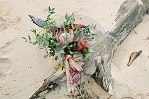 Rustic wedding bouquet with pink ribbons on the log, on the beach. Close-up. Artwork, grain