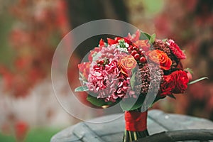 Rustic wedding bouquet with red, orange and bordeaux roses, berries, and other greens on aged wooden logs. Artwork